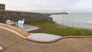 A patio with a table and chairs, a stone wall, and a view of the sea.