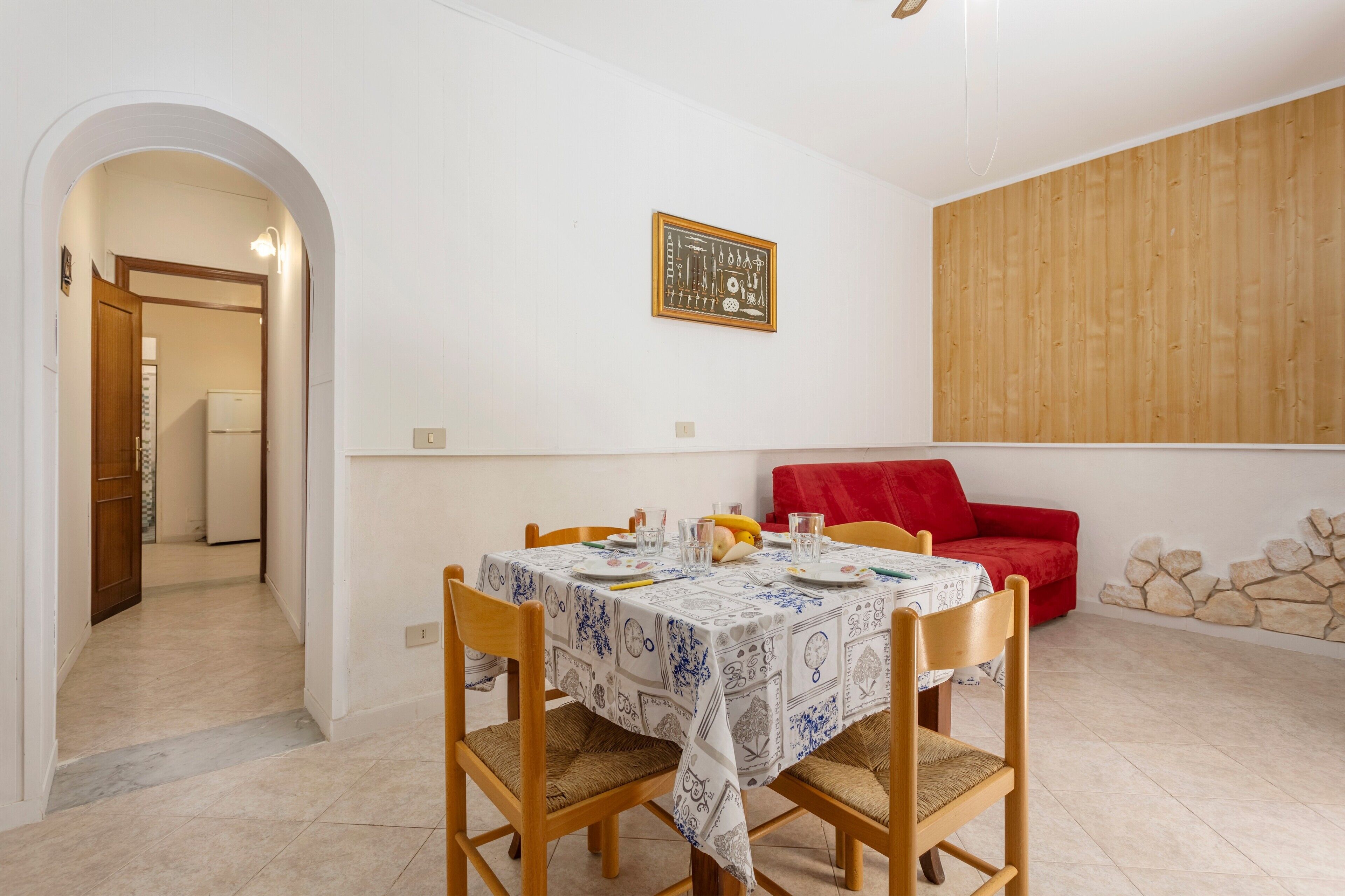 A dining area with a table set for four, a red sofa, and a wooden wall panel.