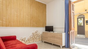 A room with a red sofa, a wooden cabinet with a television, a stone wall, and a wooden door.