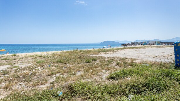 A beach with a clear sky, sandy shore, and distant mountains.