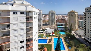 A high-rise building with balconies, a swimming pool, and a view of the surrounding cityscape.