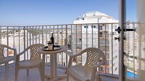 A balcony with white plastic chairs and a small table, overlooking a residential area with white buildings.