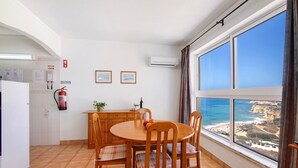 A dining area with a view of the sea, a kitchen with a refrigerator, and a fire extinguisher.