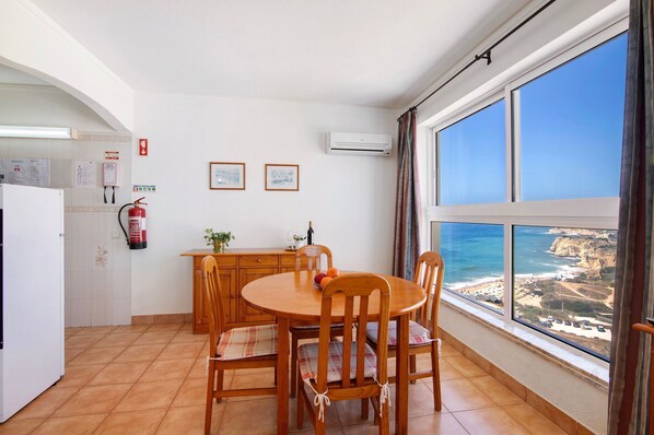 A dining area with a view of the sea, a kitchen with a refrigerator, and a fire extinguisher.