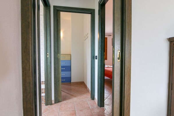 A hallway with a tiled floor leading to a room with a bed and a dresser.