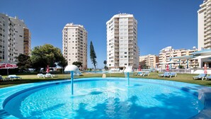 A swimming pool with lounge chairs, surrounded by high-rise buildings and a clear sky.