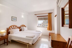 Une chambre avec deux lits, une table de chevet en bois, une table et une fenêtre avec des rideaux.