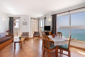 Un salon avec un canapé, une table à manger et des chaises, un téléviseur et une vue sur la mer.