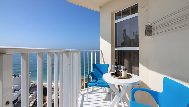 A balcony with a white railing, a table with a tray of items, and blue chairs.