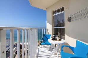Un balcon avec une balustrade blanche, une table sur laquelle se trouve un plateau rempli d’objets, et des chaises bleues.