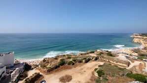 A coastal view with a beach, rocky terrain, and a building with a flat roof.