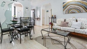Un salón con una mesa de comedor de vidrio, sillas negras, un sofá con tapicería floral, una mesa de centro y un cuadro abstracto grande en la pared.