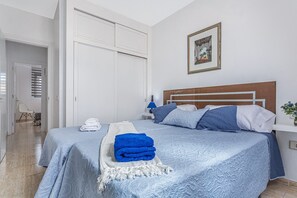 A neatly made bed with blue bedding, a white headboard, and a bedside table with a lamp.