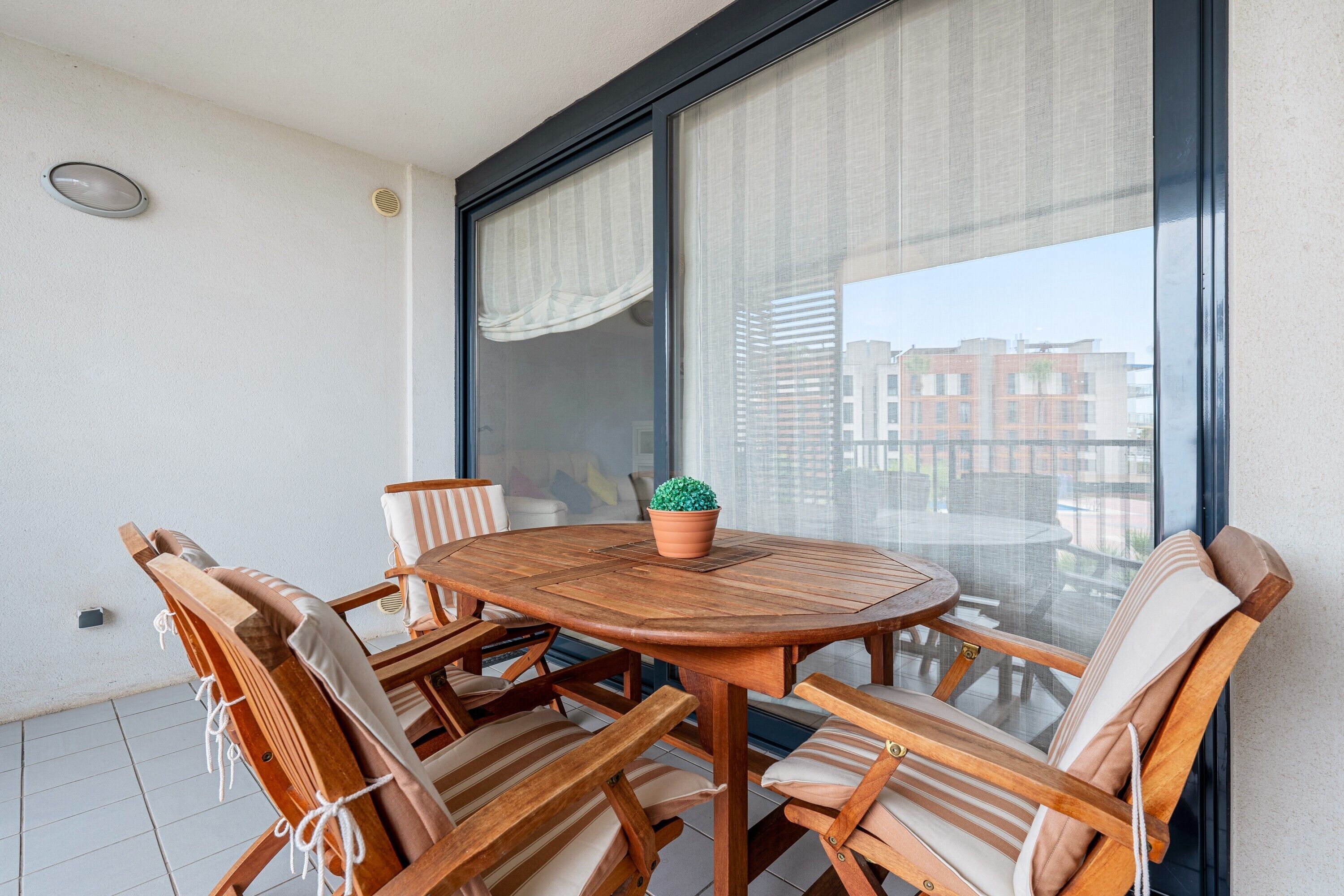 A round wooden table with six chairs, a potted plant, and a large window with curtains.