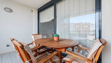 A round wooden table with six chairs, a potted plant, and a large window with curtains.