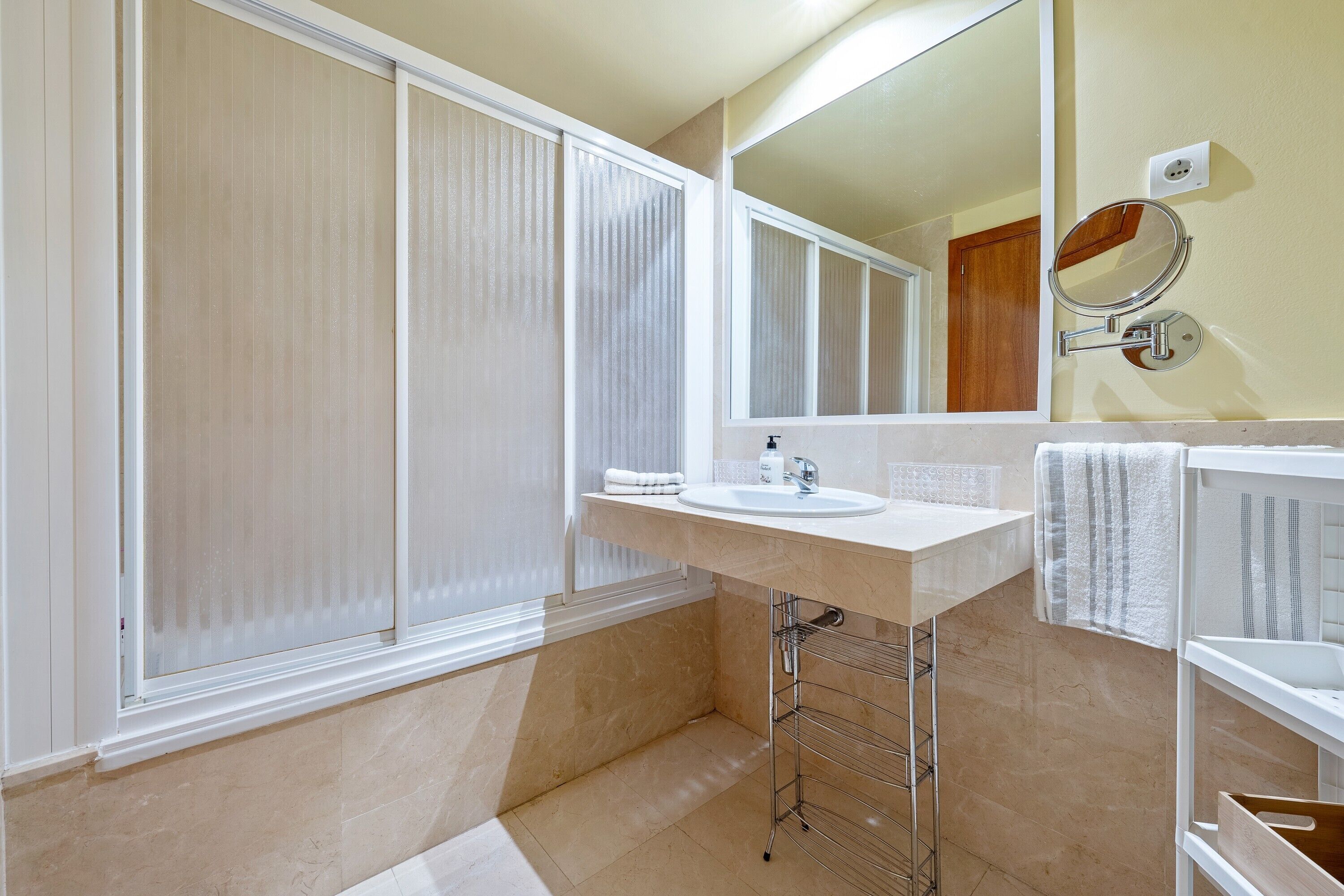A bathroom with a large mirror, a sink, a towel rack, and a shower area.