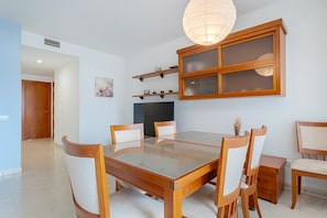 Un comedor con mesa de vidrio, sillas de madera, una alacena con puertas de cristal y una lámpara colgante.