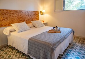 Een net opgemaakt bed met een gestreept hoofdbord, een nachtkastje met een lamp en een dienblad met een theepot en kopjes.