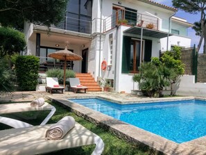 Una casa moderna de dos pisos con piscina, mobiliario exterior y una escalera que lleva al piso superior.