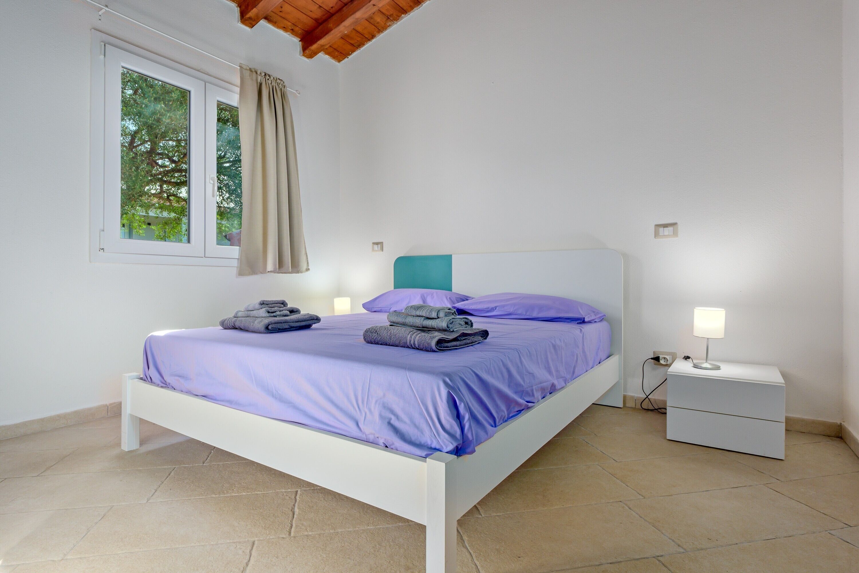 A bedroom with a bed, a nightstand, a lamp, and a window with curtains.