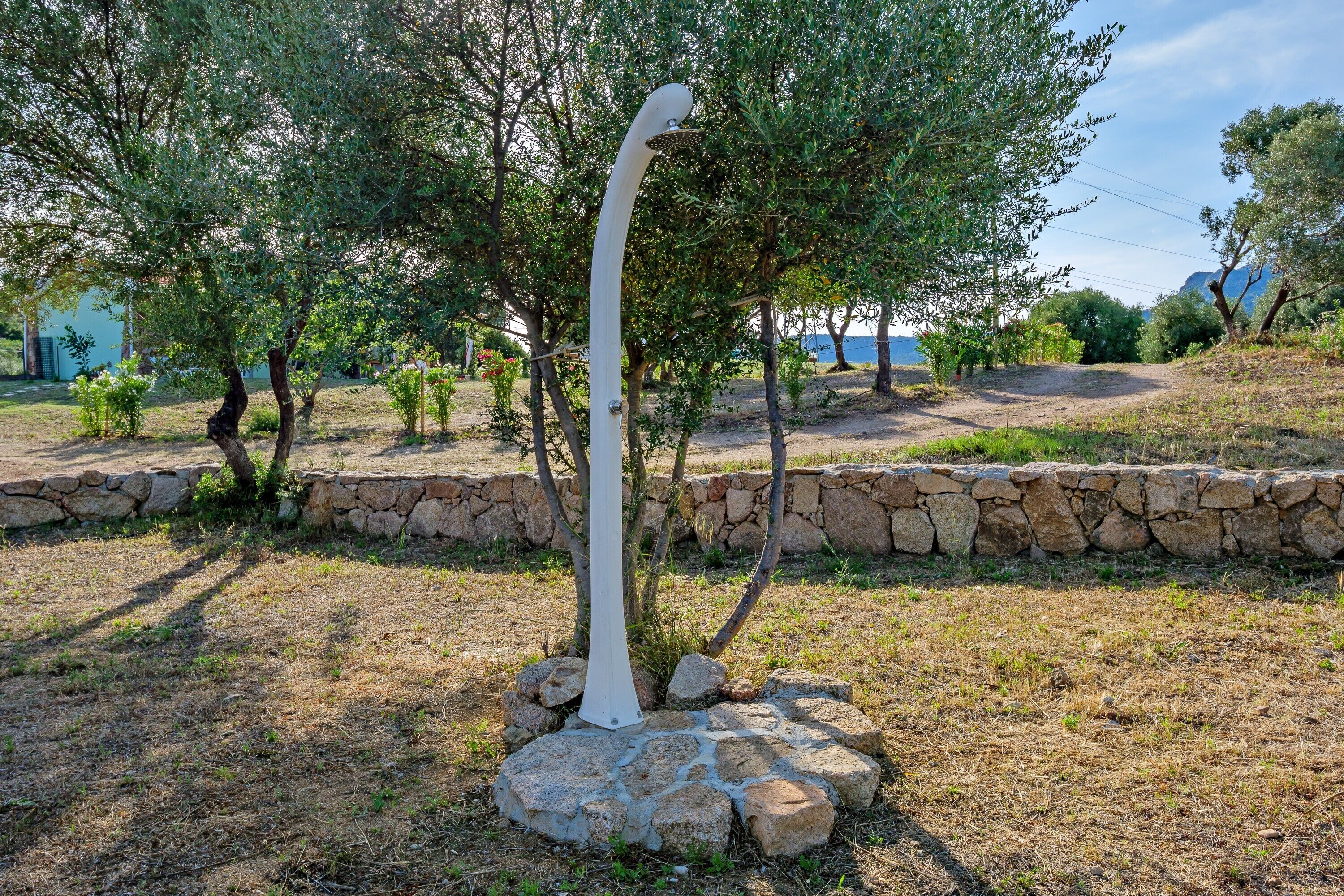 A garden with a white sculpture, stone wall, and trees.