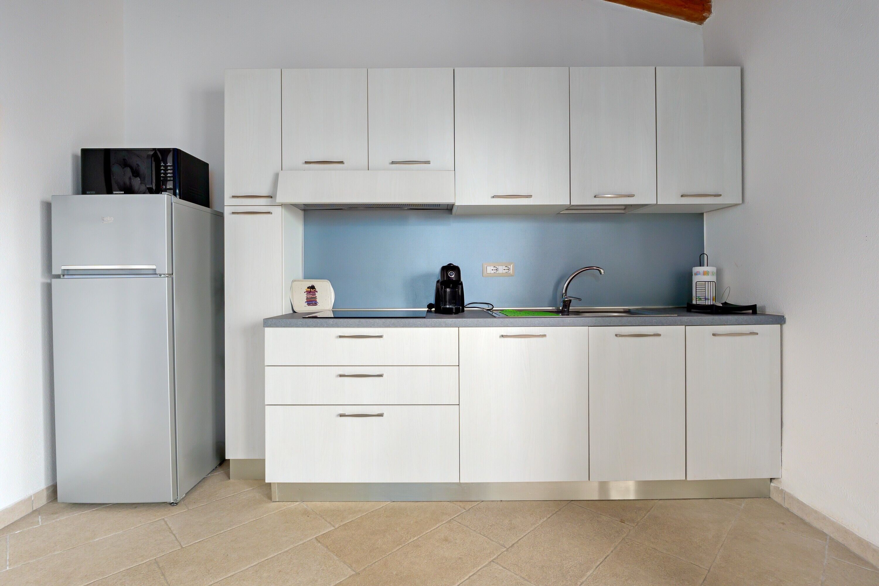 A kitchen with white cabinets, a grey refrigerator, a coffee maker, and a kettle.