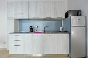 Une cuisine avec des meubles de couleur bois clair, un réfrigérateur en acier inoxydable, un four à micro-ondes, une machine à café et un évier.