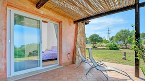 Un patio cubierto con una puerta corrediza de vidrio que da a un dormitorio con una colcha morada.