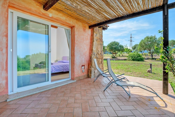 Une terrasse couverte avec une porte-fenêtre coulissante donnant sur une chambre où se trouve un couvre-lit violet.