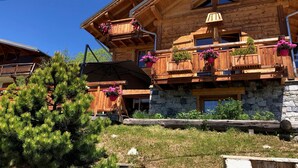 Eine Holzhütte mit Balkonen, Steinmauern und blauem Himmel.