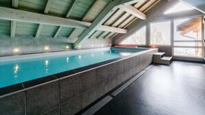Ein Schwimmbecken mit einer gefliesten Kante, Holzbalken und Blick durch große Fenster.