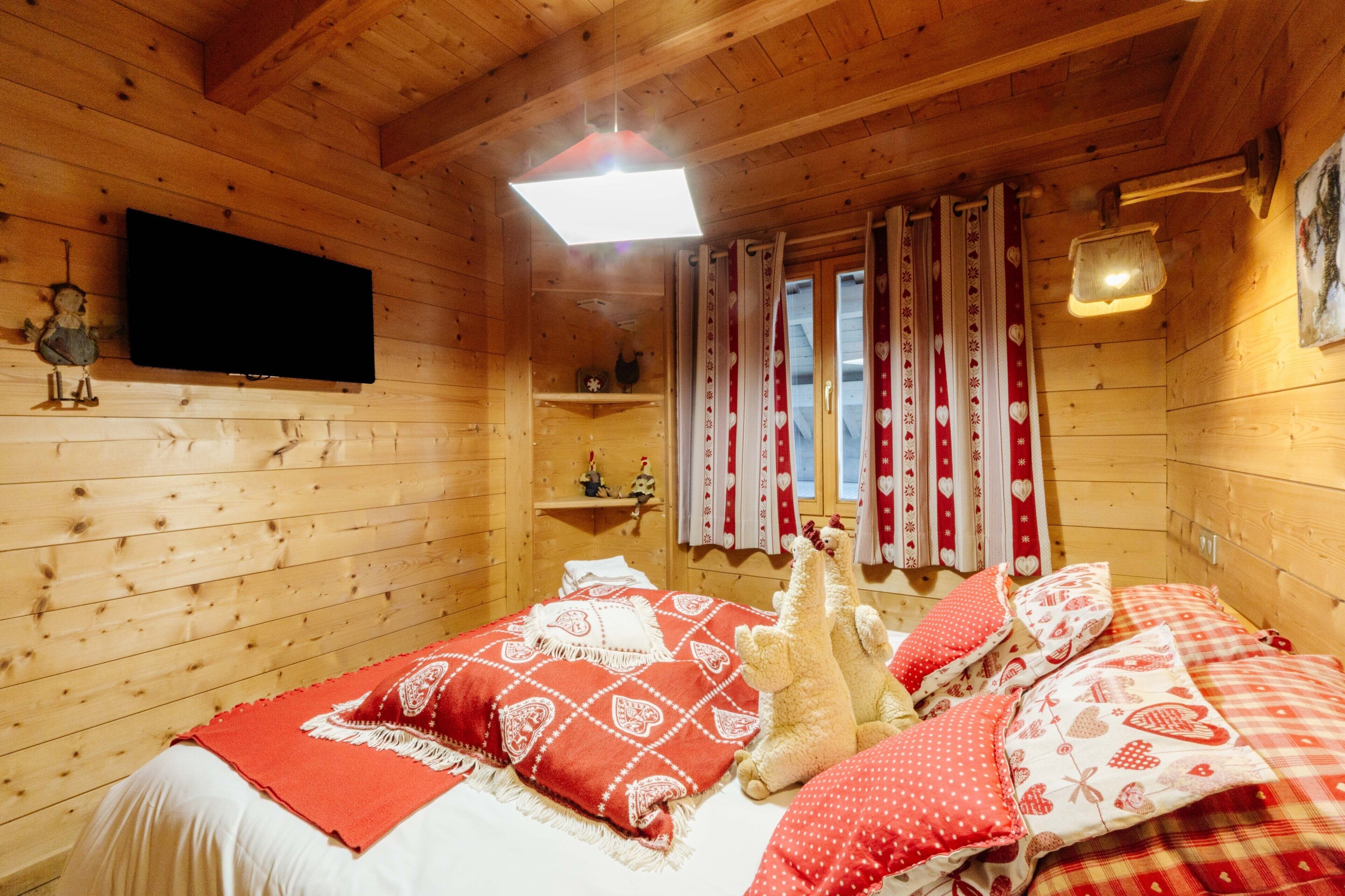 Un dormitorio de cabaña de madera con cama, almohadas, televisor y cortinas.