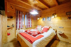 Una habitación de cabaña de madera con una cama, un estante con adornos, una ventana con cortinas y luces fijadas a la pared.