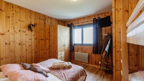 A wooden-paneled room with a bed, a radiator, a window, and a ski rack.
