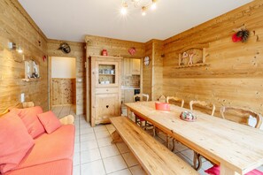 A wooden interior with a dining table, benches, a sofa, and a kitchen area. - Apartment 'Sabot De Vénus' with Mountain Views, Shared Garden & Wi-Fi (Fontcouverte-la-Toussuire)