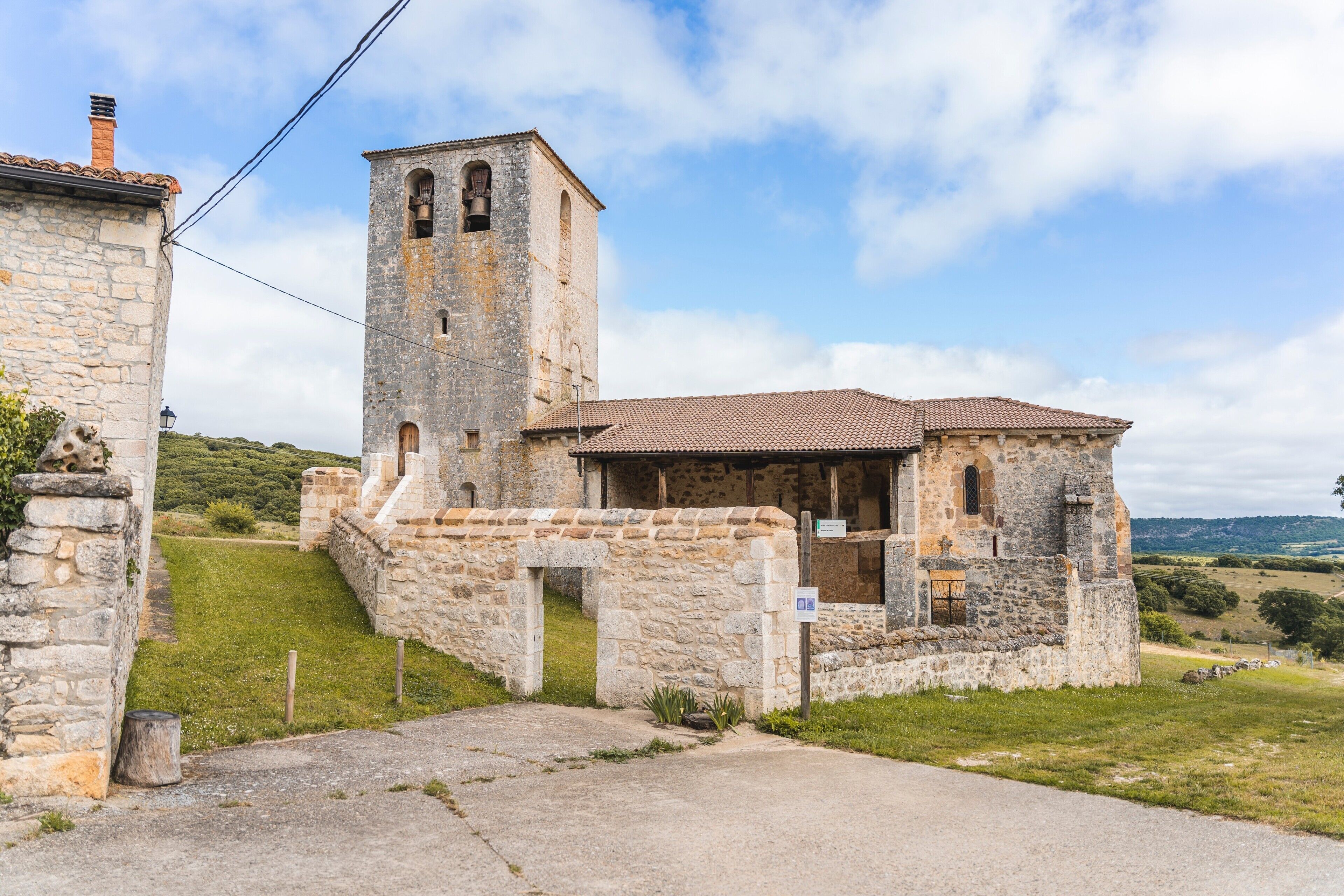 A stone church with a bell tower, a small entrance, and a paved pathway leading to it.