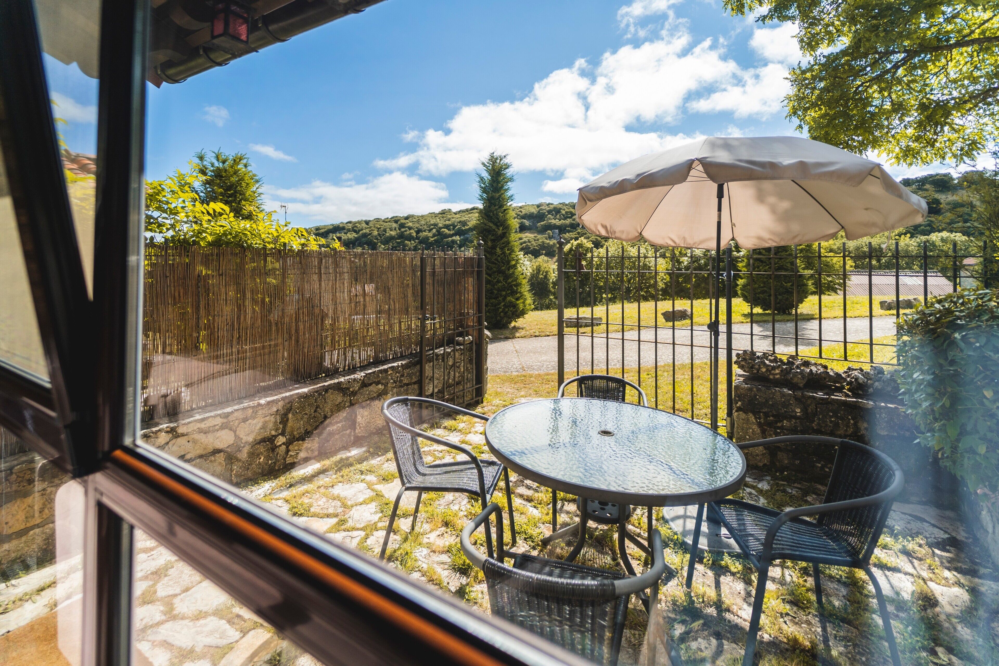 Une terrasse avec une table ronde et des chaises, un parasol, et une vue sur un chemin de pierres et de la verdure.
