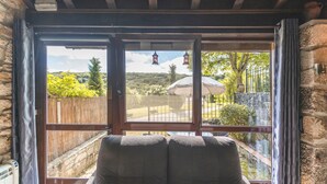 Ein Zimmer mit einem großen Fenster, einer Holztür und Blick auf einen Garten mit Zaun, Bäumen und einem Wasserfall.