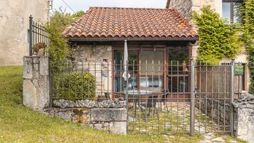 Un edificio rústico con tejado de tejas, una reja de metal y un muro de piedra.