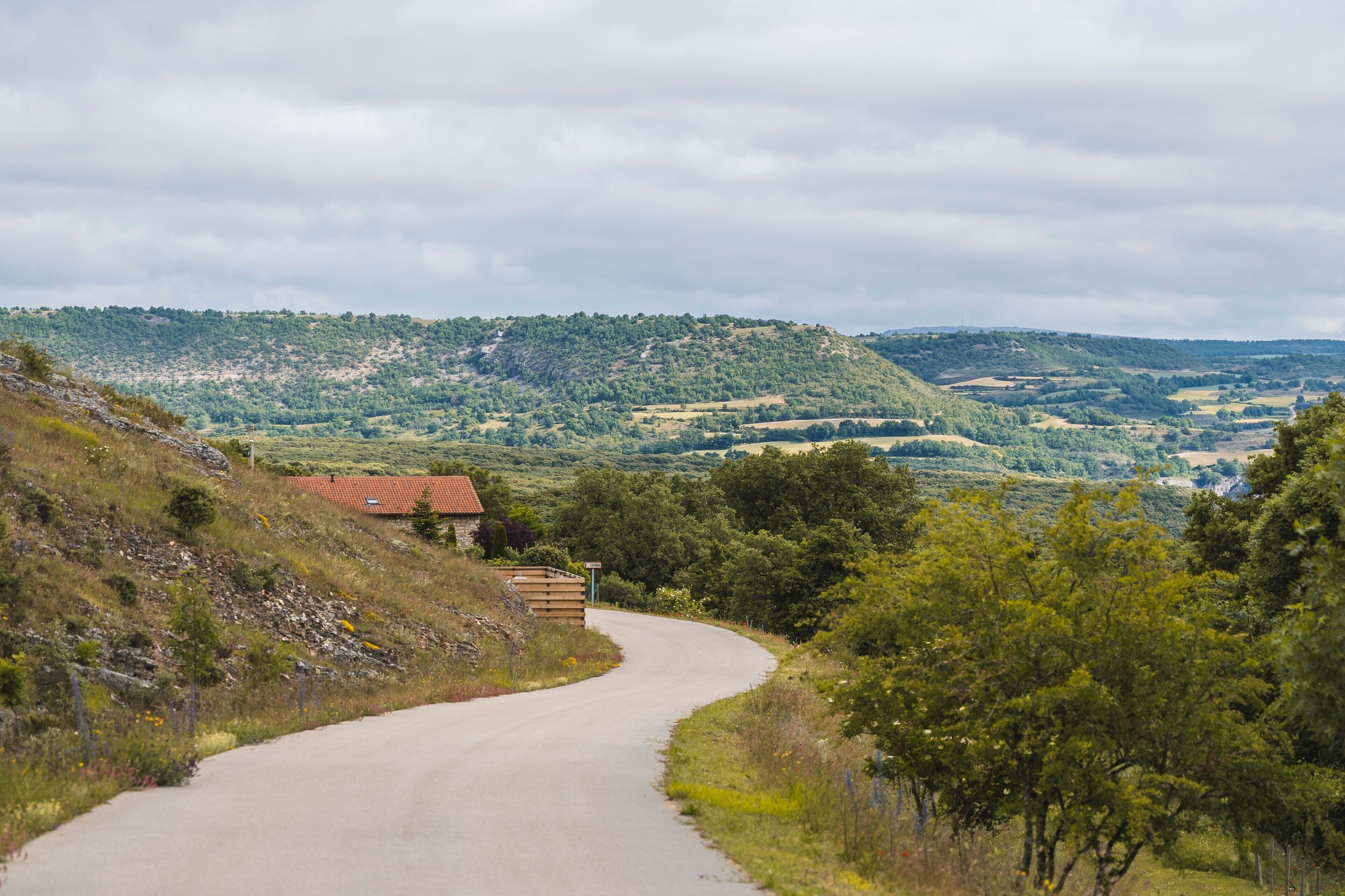 Un camino rural serpentea por un paisaje montañoso, con un pequeño edificio a la izquierda.