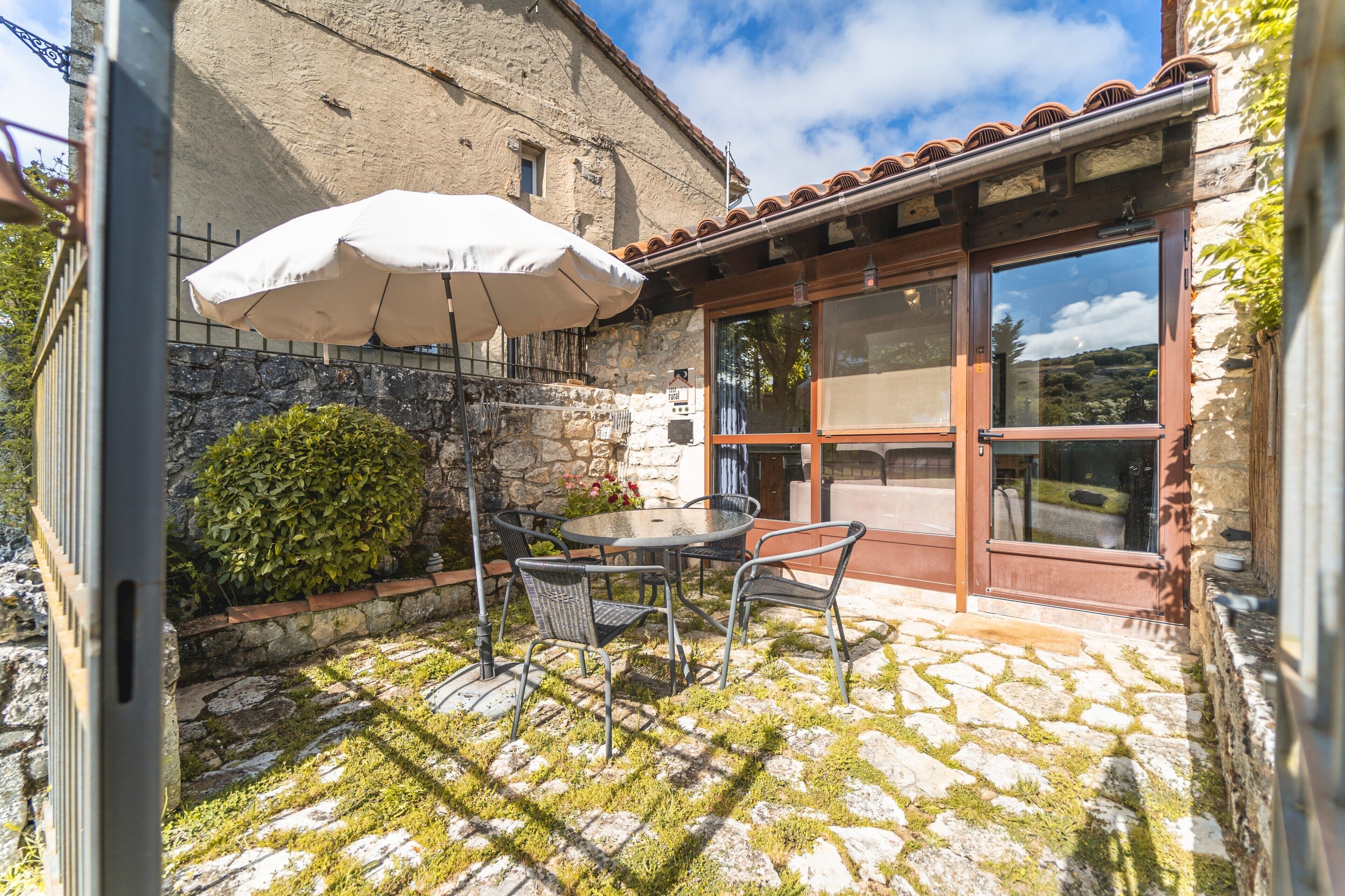 A stone patio with a table and chairs, a white umbrella, and a view of a stone building.