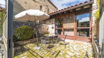A stone patio with a table and chairs, a white umbrella, and a view of a stone building.