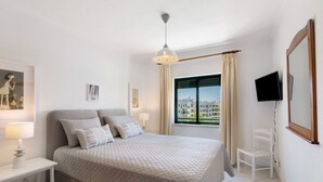 A bedroom with a bed, bedside tables, a TV, a chair, and a window with a view. - Apartment 'Vila Armação de Pêra' with Shared Pool, Wi-Fi and Air Conditioning (Armação de Pêra)
