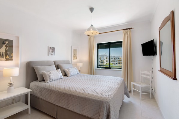 Une chambre à coucher avec un lit, des tables de chevet, une télévision, une chaise et une fenêtre donnant sur un beau paysage.