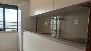 A modern kitchen with white cabinets, a stainless steel sink, and a window overlooking a residential area. - Apartment 'Vila Armação de Pêra' with Shared Pool, Wi-Fi and Air Conditioning (Armação de Pêra)