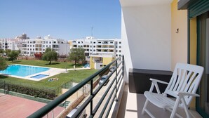 A balcony with a white chair, a swimming pool, and a view of a residential area. - Apartment 'Vila Armação de Pêra' with Shared Pool, Wi-Fi and Air Conditioning (Armação de Pêra)