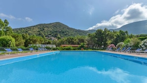 A clear blue swimming pool with lounge chairs and a mountain backdrop.