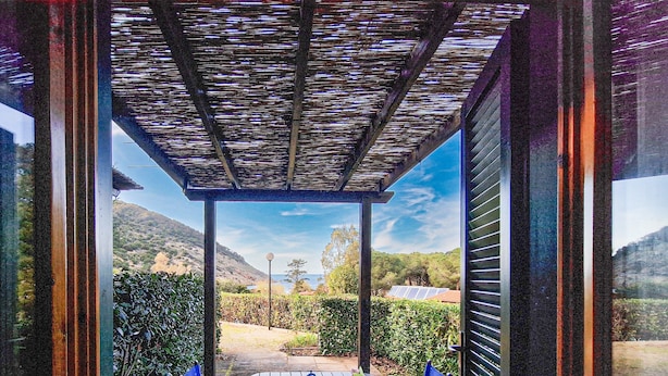 A covered patio with a table and chairs, a view of a mountainous landscape, and a building with a sloped roof.