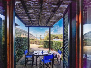 A covered patio with a table and chairs, a view of a mountainous landscape, and a building with a sloped roof. - Apartment 'Altaluna with Pool' with shared pool, private terrace and balcony (Nisporto)