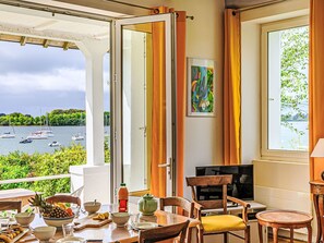 A dining area with a view of boats on a lake, a painting on the wall, and a table set with various dishes. - Maison La Prâme by Interhome (Arradon)